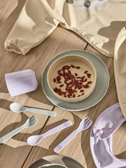 Children's tableware set with bowls, spoons, and forks on a wooden surface.