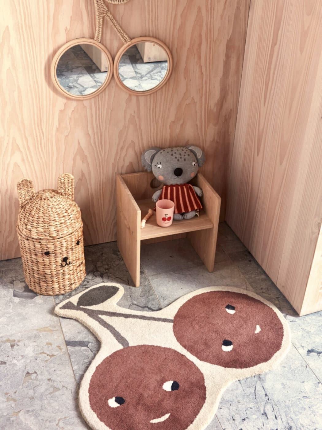 Children's room with wooden shelf, teddy bear, and cherry-themed rug.