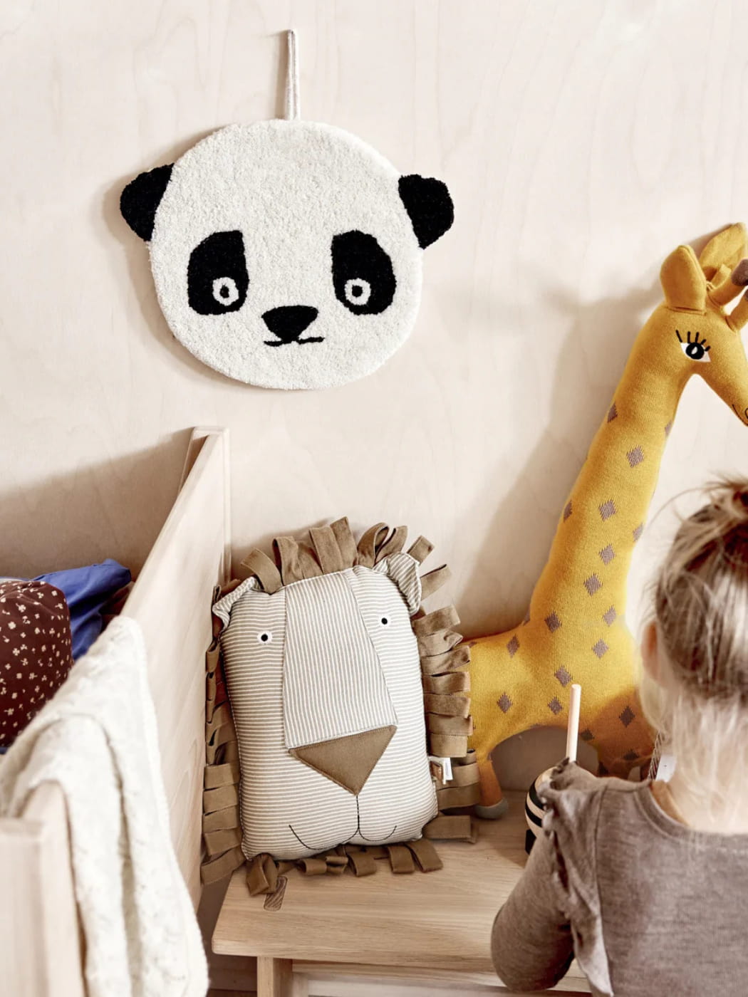 Children's room with a panda-shaped pillow, lion pillow, and giraffe plush toy.