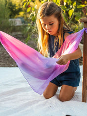 Young girl playing with a pink and purple silk outdoors.