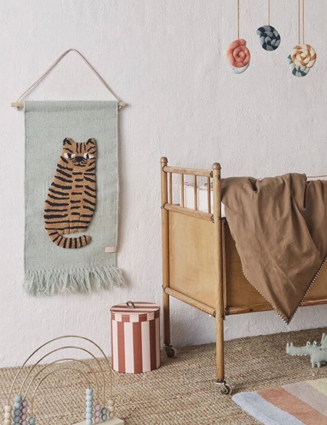 Nursery room with a tiger wall hanging, crib, and colorful mobile.
